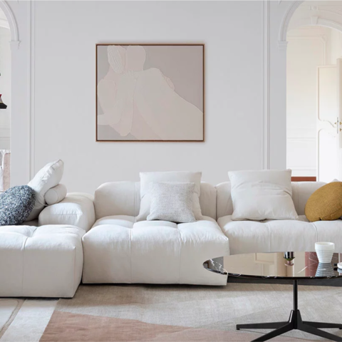 Immagine di un salotto di Saba, cliente di Extera che ha implementato un Dam. L'immagine mostra un divano bianco molto ampio con cuscini, sotto un tappeto dai colori tenui sul beige e il rosa e un quadro sulla parete dietro il divano con un disegno stratto.